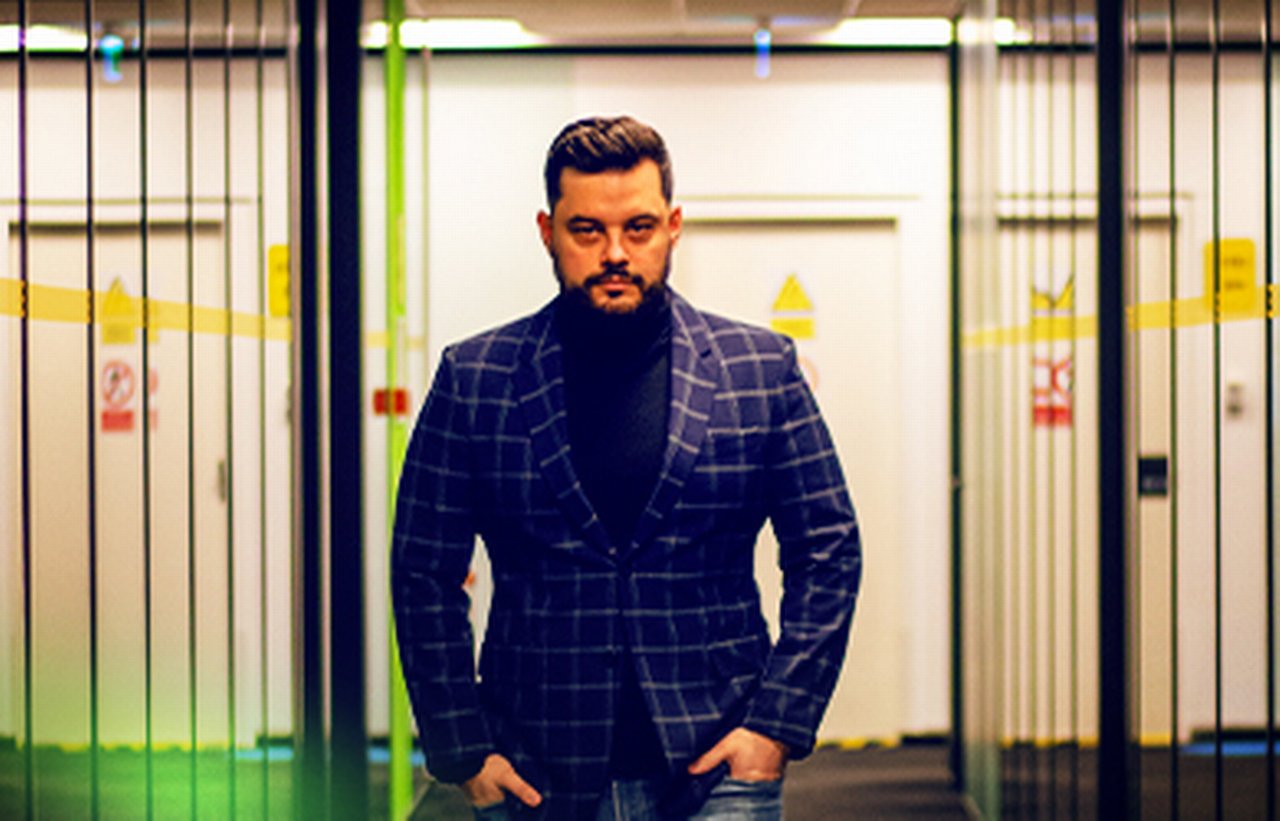 Mihai steht in einer offenen Tür. Er trägt einkariertes Sakko.