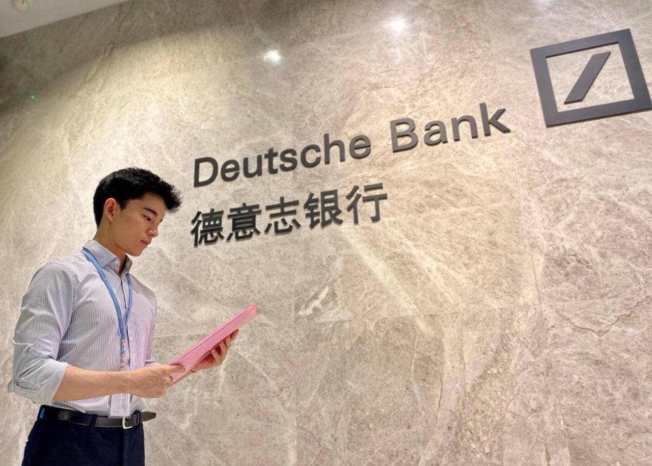 Sean in front of a wall with the Deutsche Bank China logo