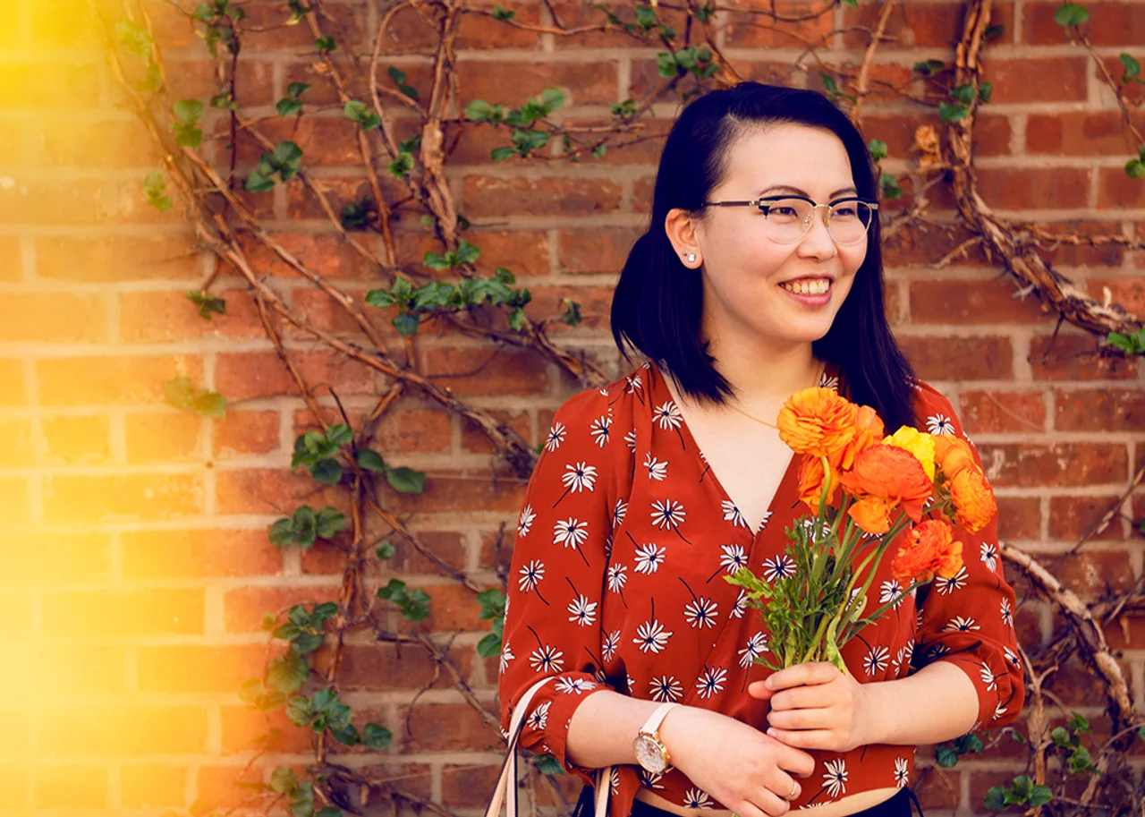 Tina mit einem Blumenstrauß vor einer berankten Steinmauer