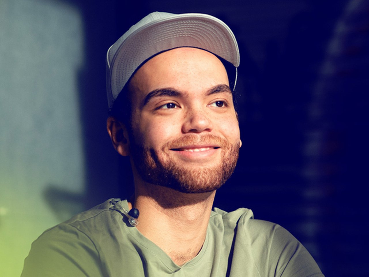 Man in military green shirt and a baseball hat smiling