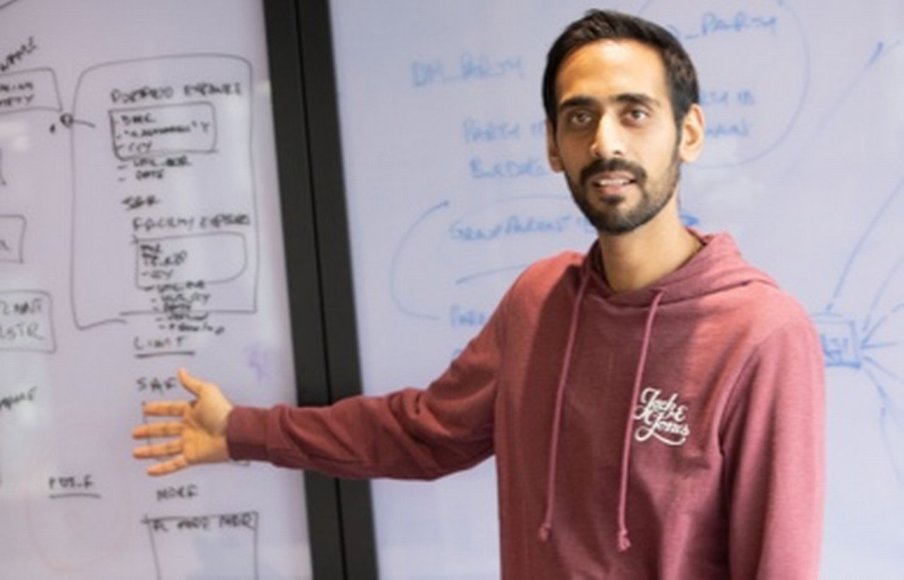 Dipesh points to a whiteboard with a lot of text written on it