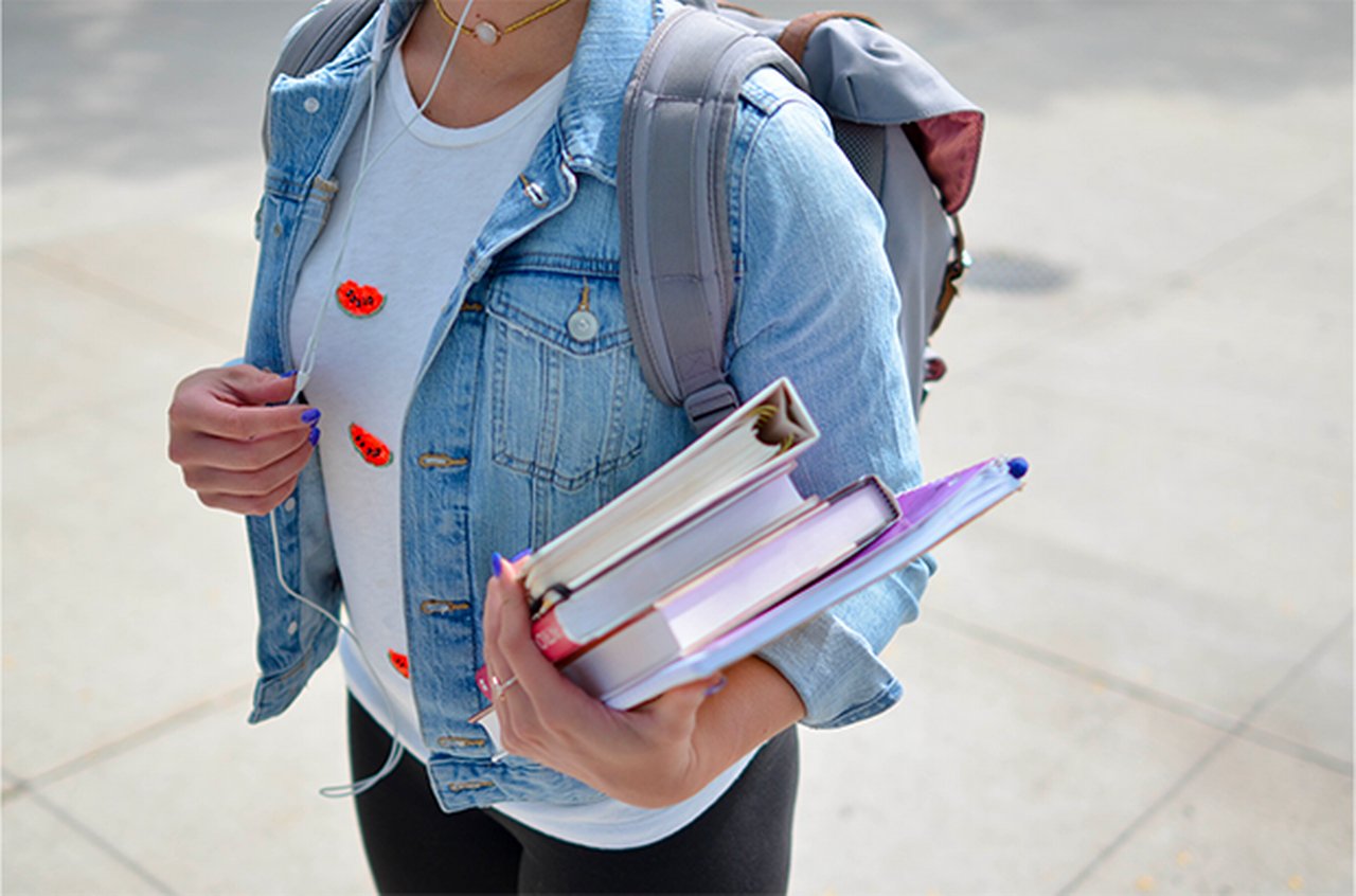 A woman with a backpack and folders and books in hand