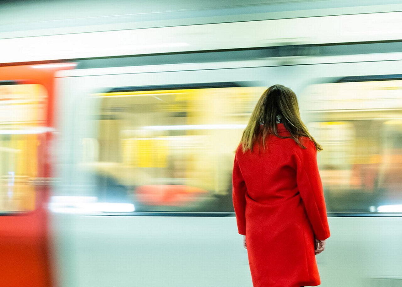 Sarah steht auf einem Bahnsteig vor einer fahrenden U-Bahn