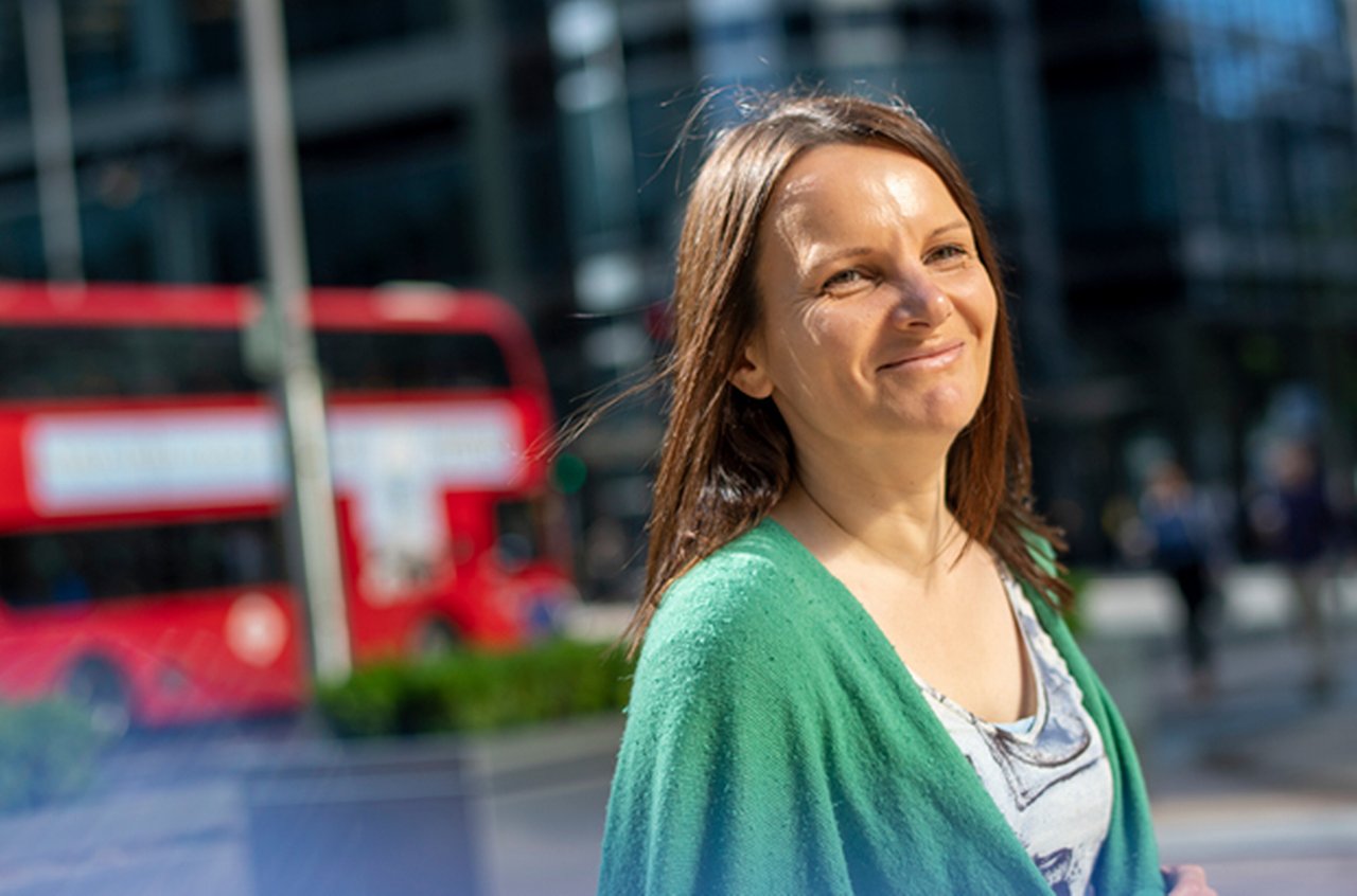 Smiling woman in green shirt. In the background is a red London bus