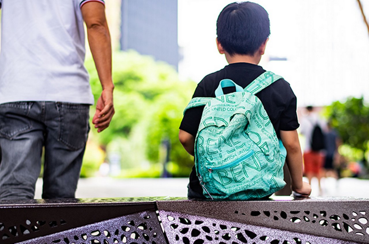 Little boy with backpack sits on a bench