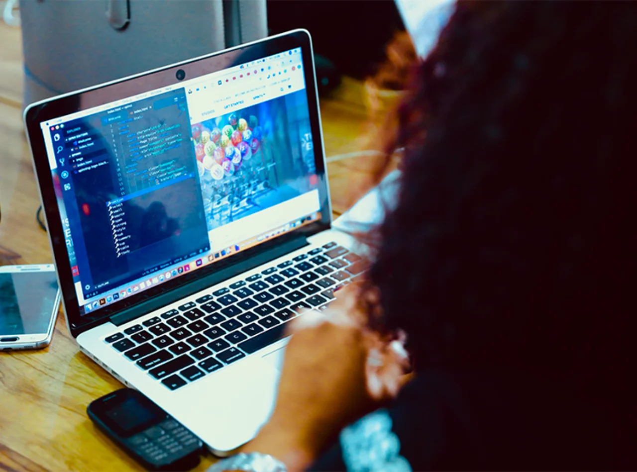 A woman from behind with her laptop open; code can be seen on the screen