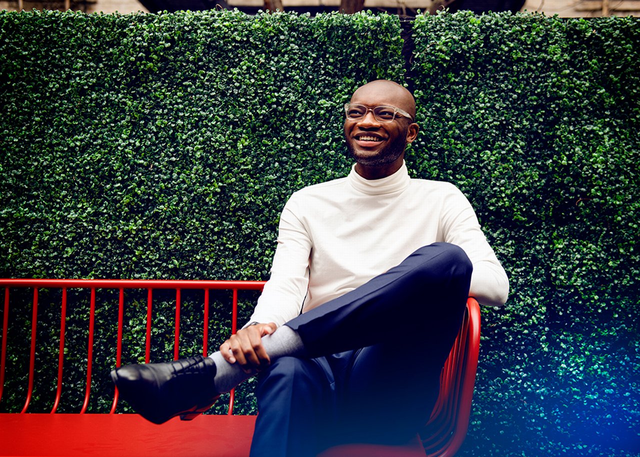 Kofi sits on a red bench in front of a box hedge