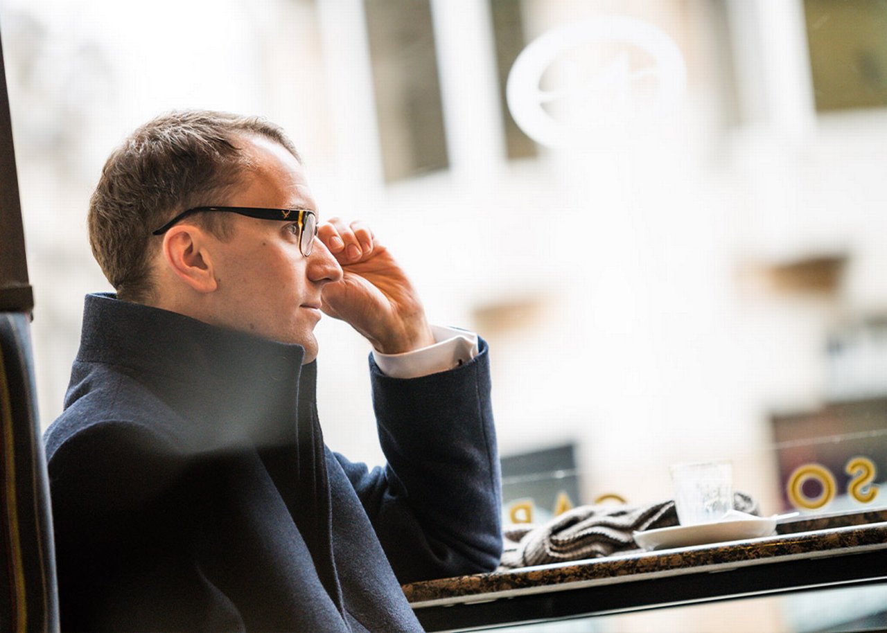 Mike is sitting in a cafe and adjusting his glasses