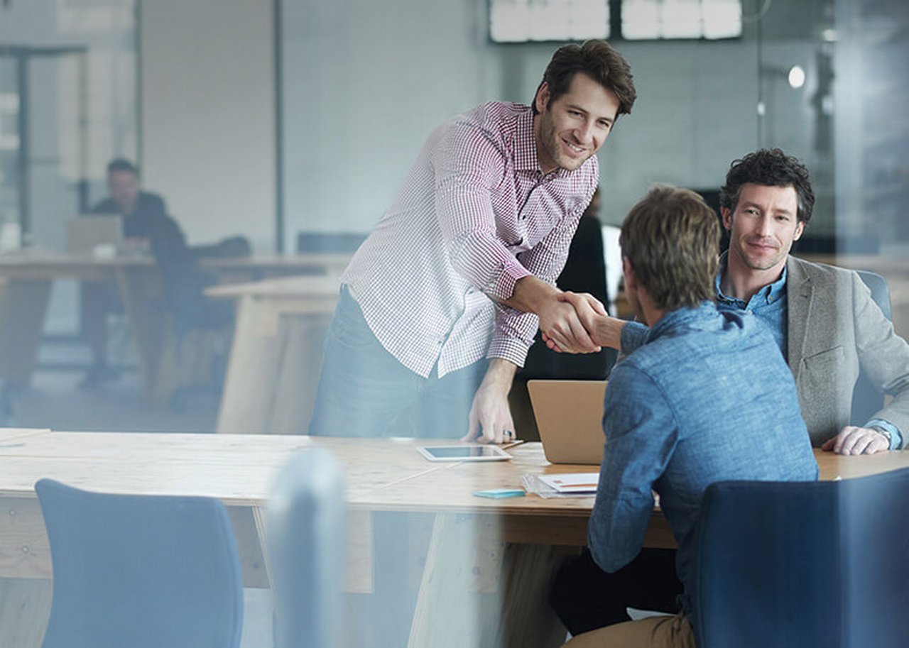 Behind a pane of glass in the office, people shake hands