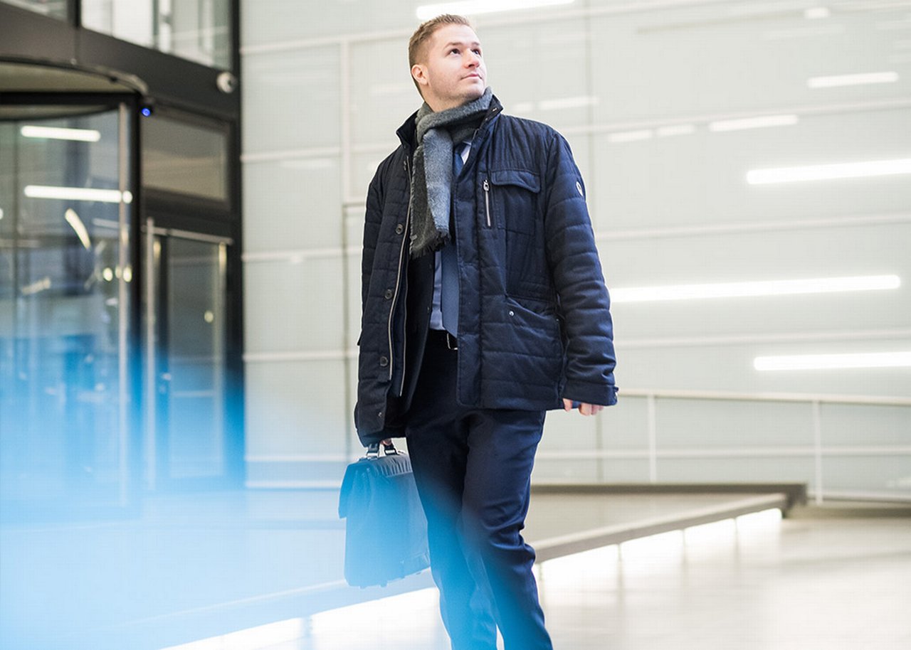Stevan is walking in a foyer with a briefcase in his hand glancing upwards