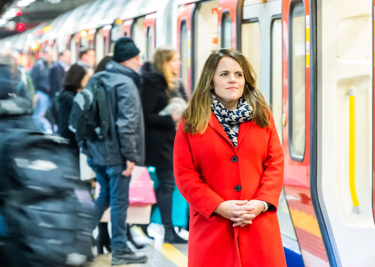 Sarah is standing on a tube station platform in front of a tube opening its doors