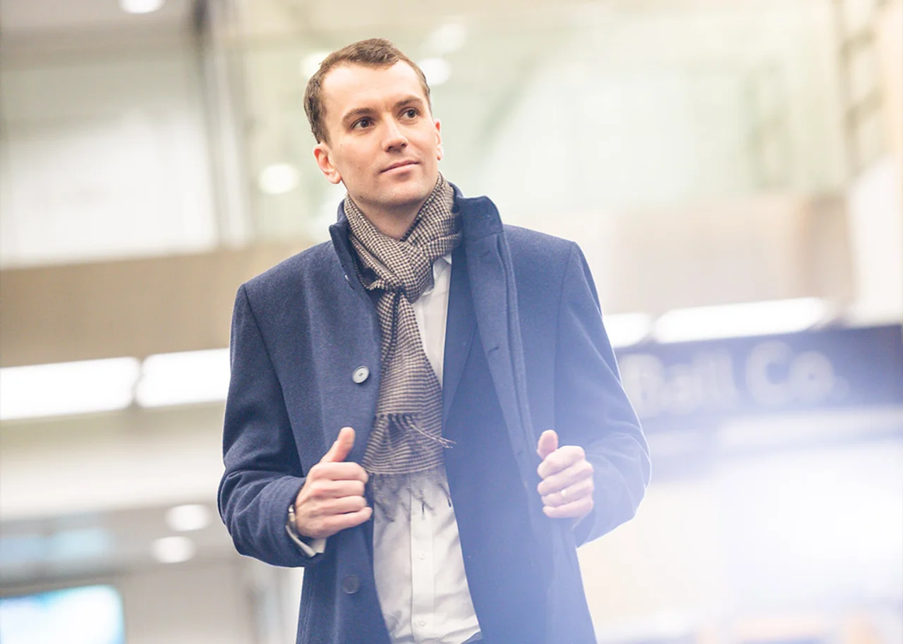 Mike steht in einem Foyer und posiert mit den Händen vor ihm