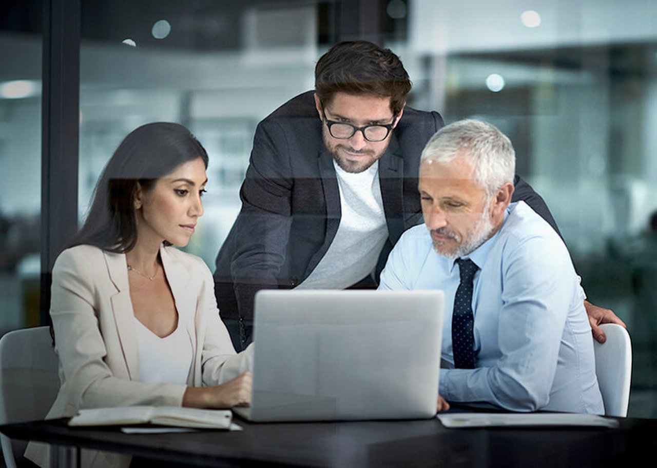 Three people are looking at something on a laptop