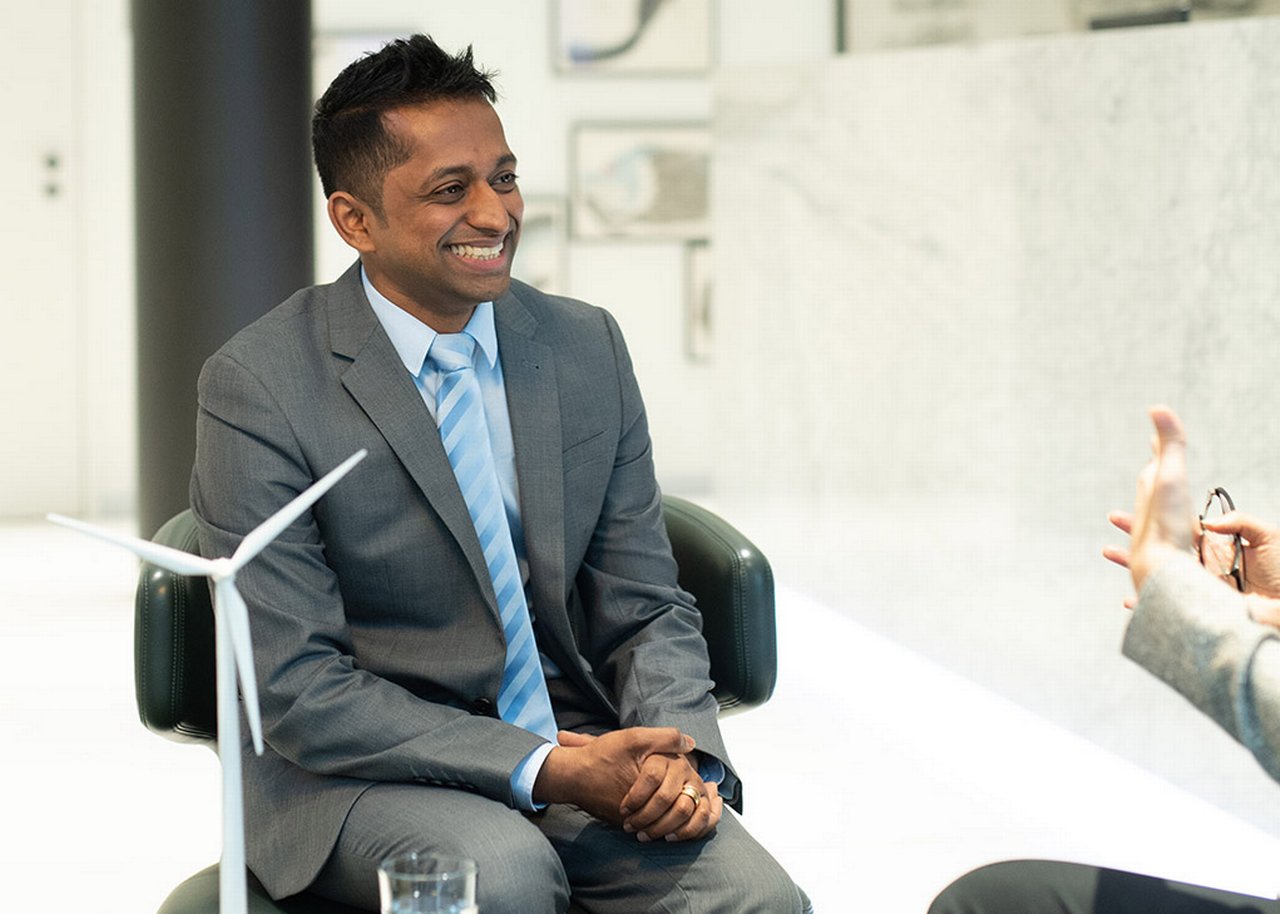 Janagran smiles during a conversation and is sitting next to a model wind turbine