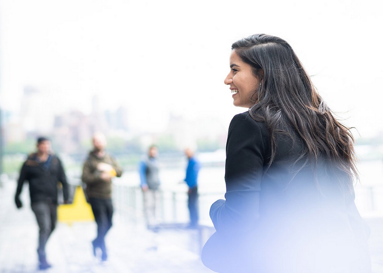 Monica is standing out in the open smiling with her back partially turned
