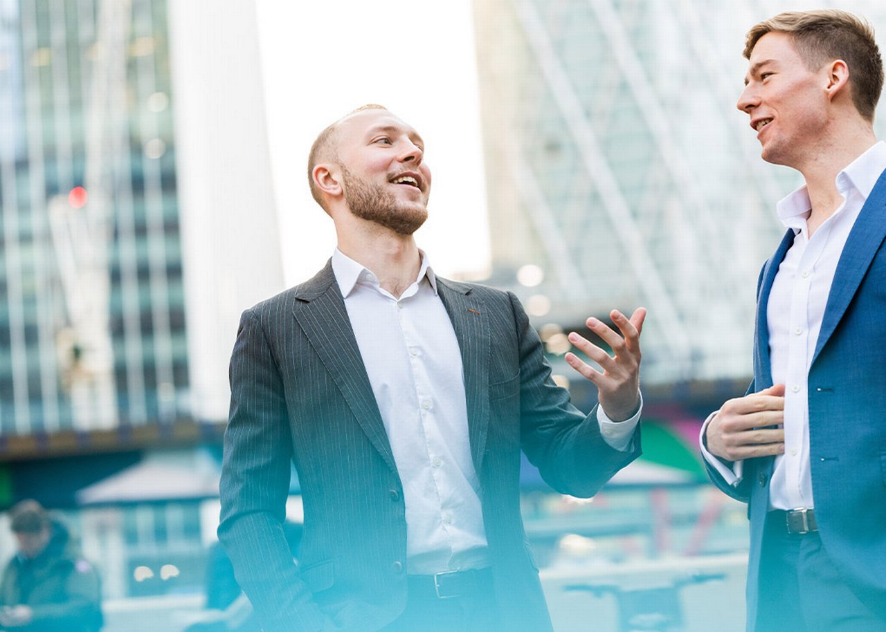 German is outside smiling in a conversation with a colleague