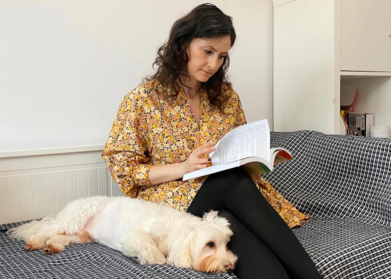 Ramona reading a book on her bed next to her dog.