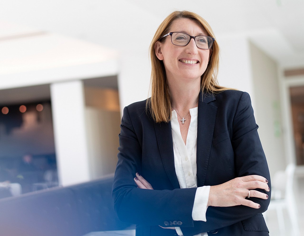 Deirdre is standing in the office with her arms crossed smiling