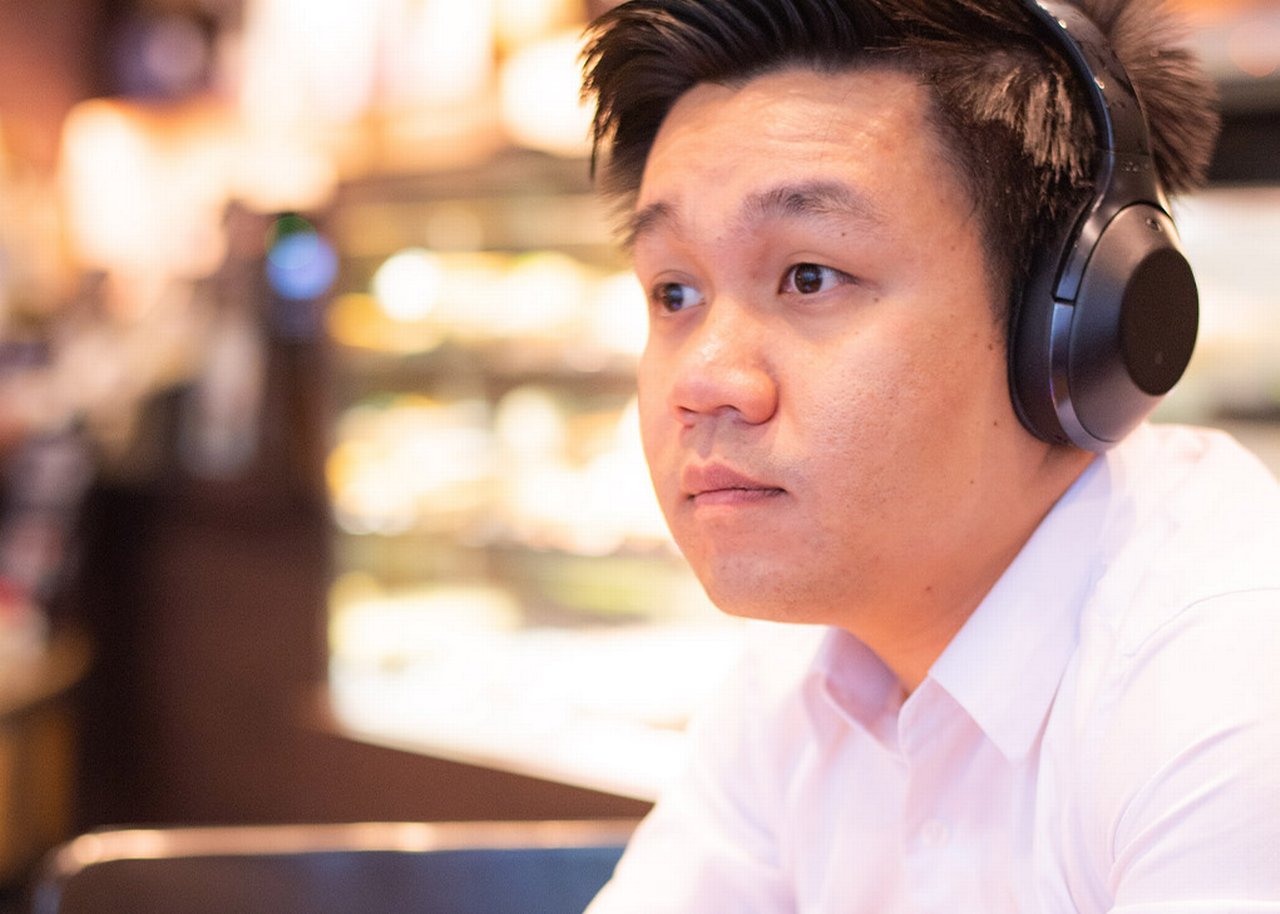 Melvyn is sitting at a desk with headphones on looking pensive