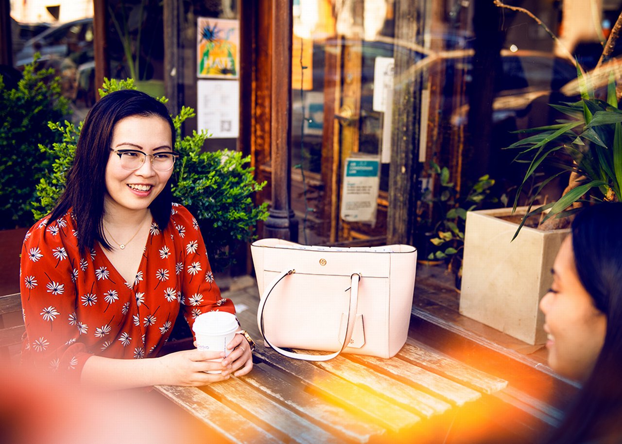 Tina and a colleague are sitting at a table with plants in front of a cafe