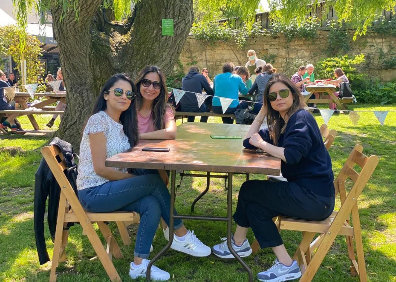 Syda is sitting with friends at a table under a tree, everyone is wearing sunglasses