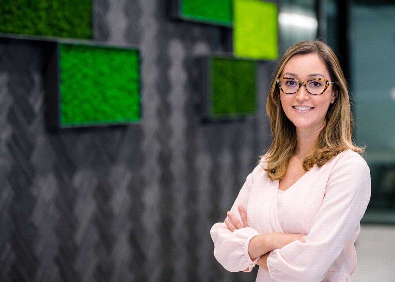 Marina smiles with crossed arms in front of a wall with modern green pictures