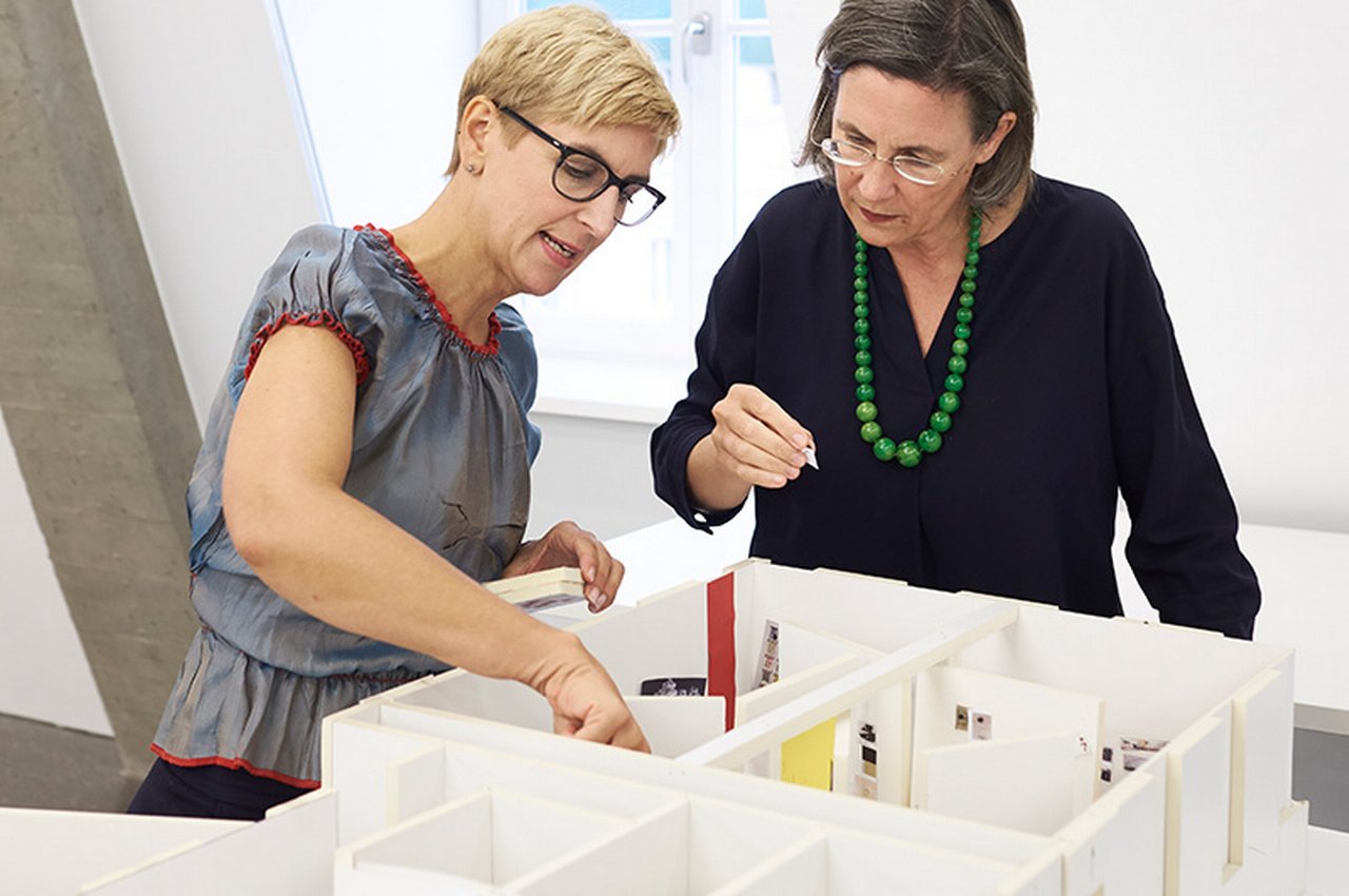 Two women are repositioning things in a model house
