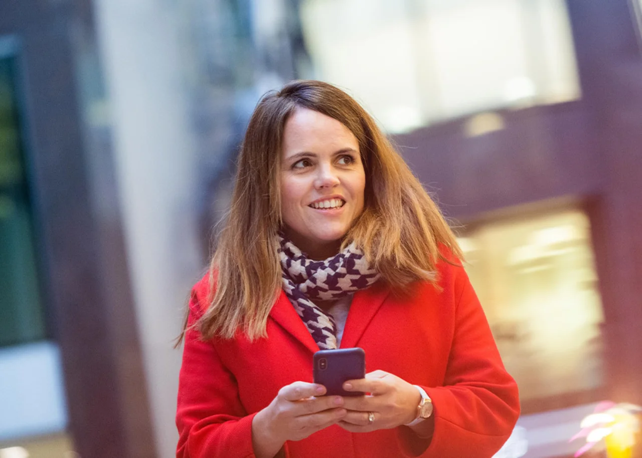 Sarah steht draußen und lächelt mit einem Handy in der Hand