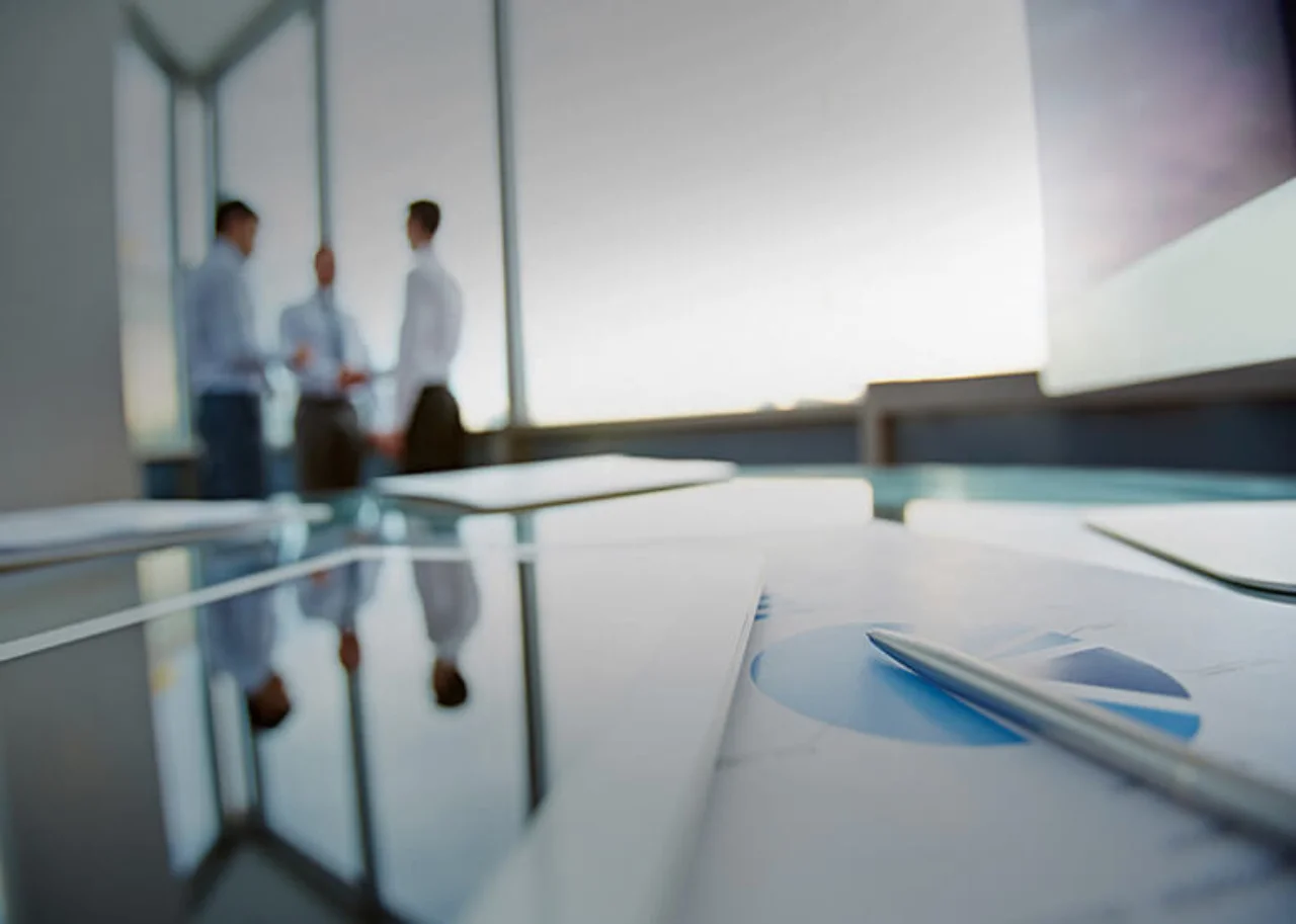 Three people are reflected in a large glass table