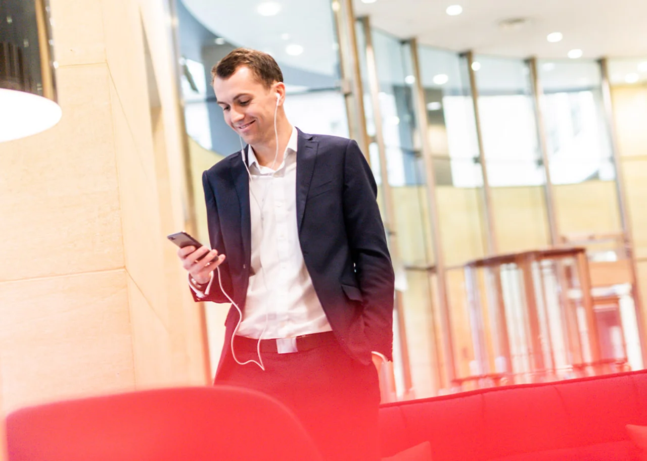 Mike is standing in a foyer smiling with his phone in his hand and with headphones on