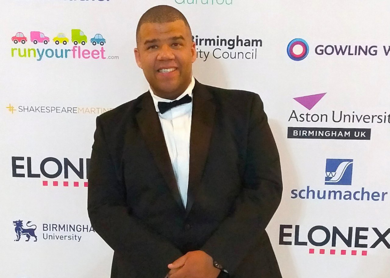 Tim George in suit in front of wall with logos