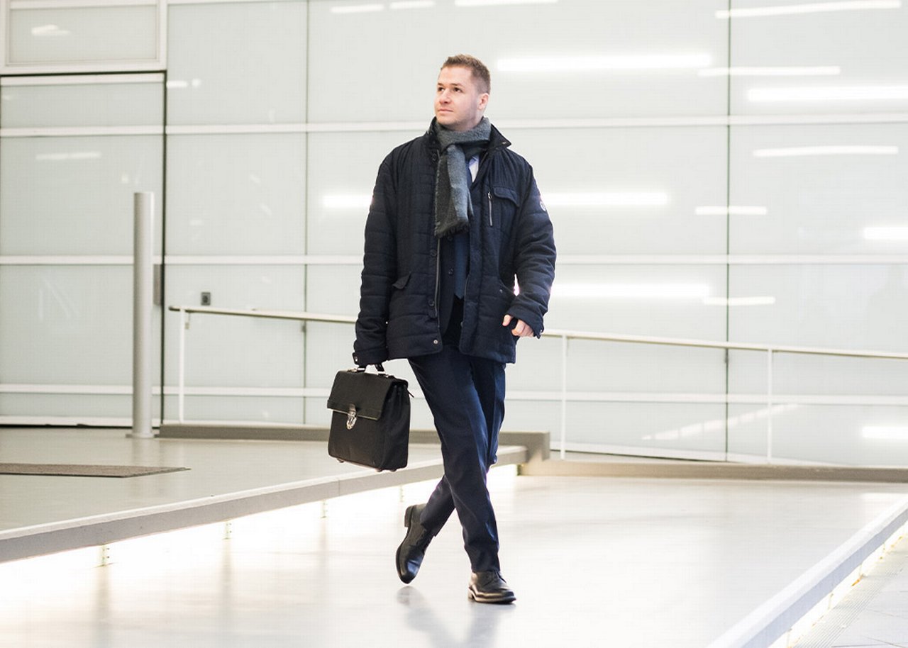 Stevan is walking through a foyer with a briefcase in his hand glancing to his right
