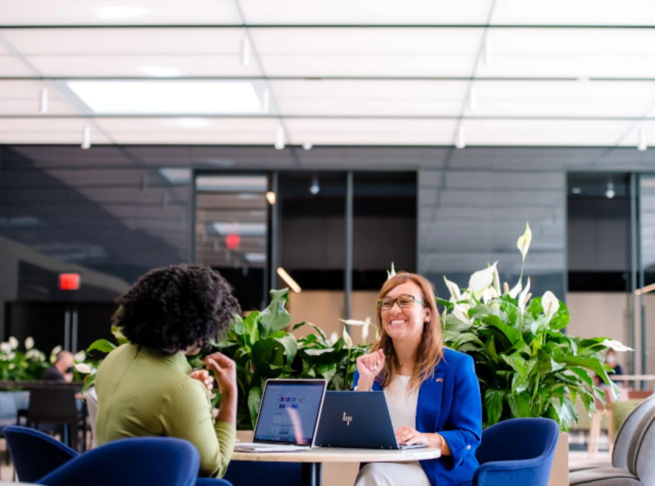 two women with laptop sitting at a table and laughing