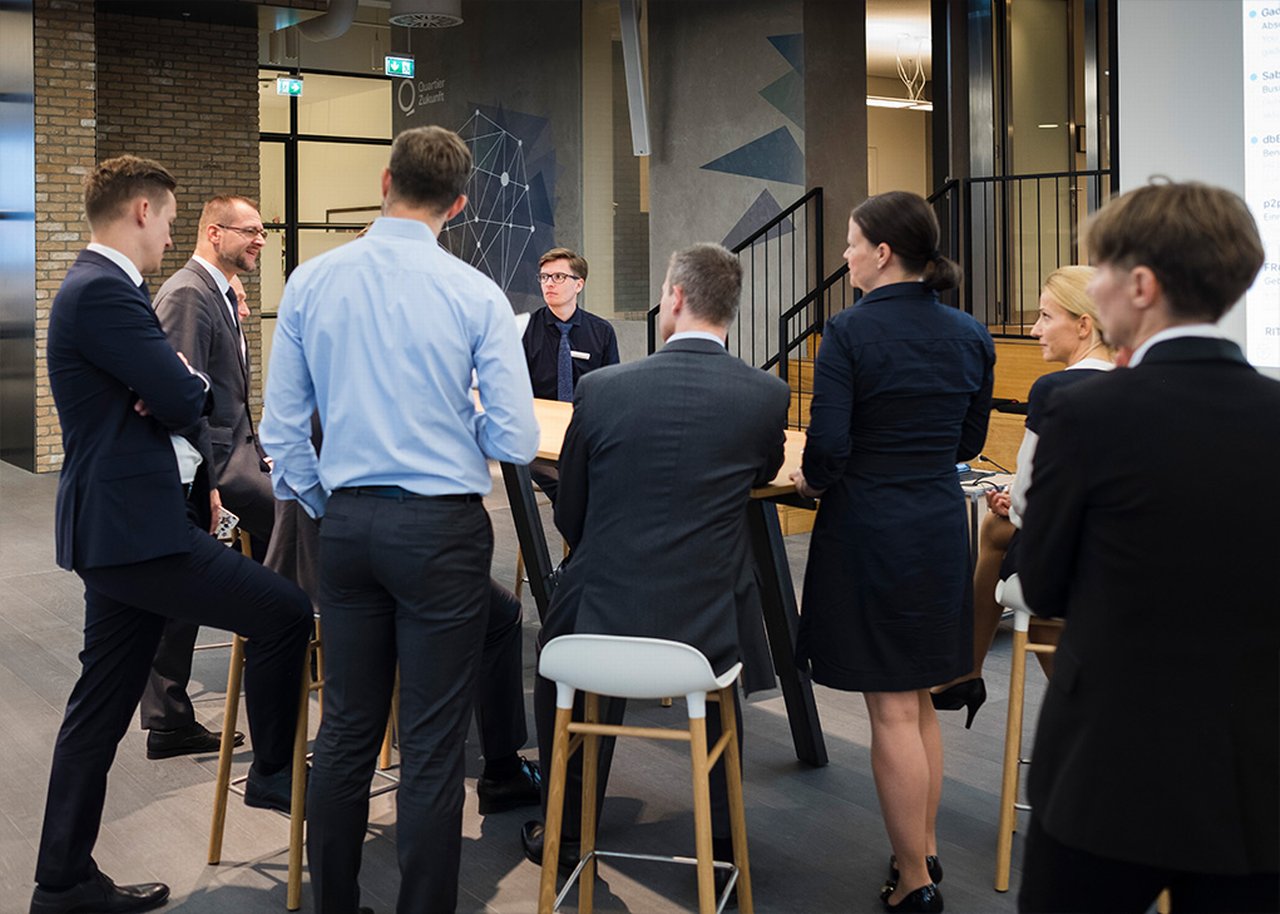 Alexander is standing around a table with colleagues having a discussion