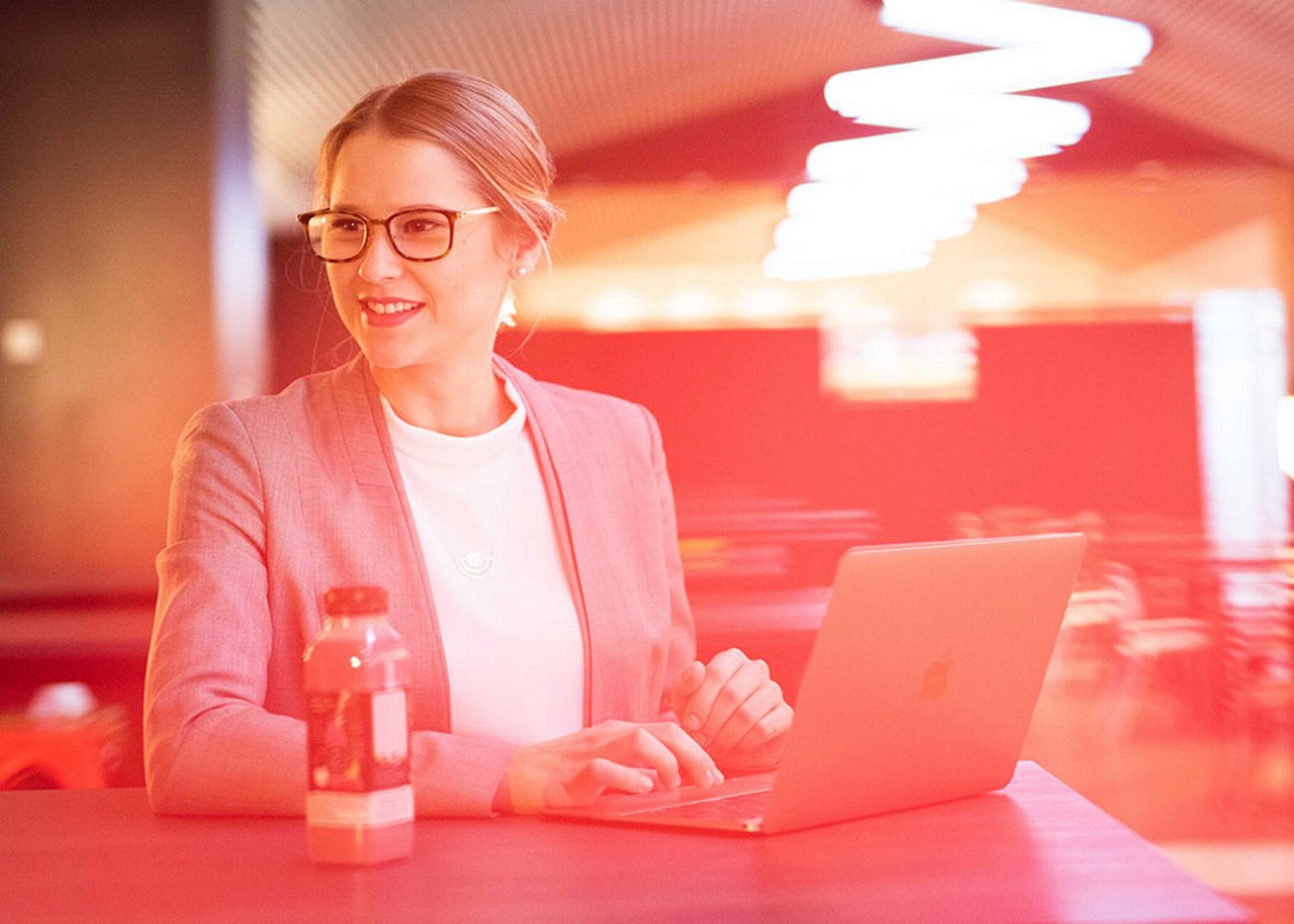 Manuela sitzt an einem Tisch vor ihrem Laptop und lächelt
