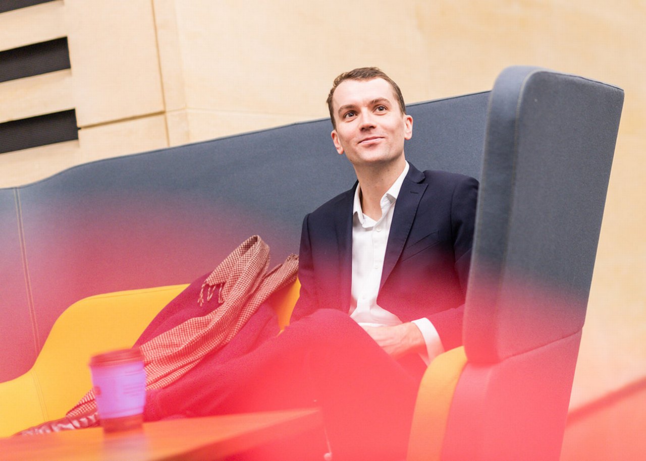 Mike sitzt auf einem Sofa mit einer Tasse Kaffee auf dem Tisch vor ihm