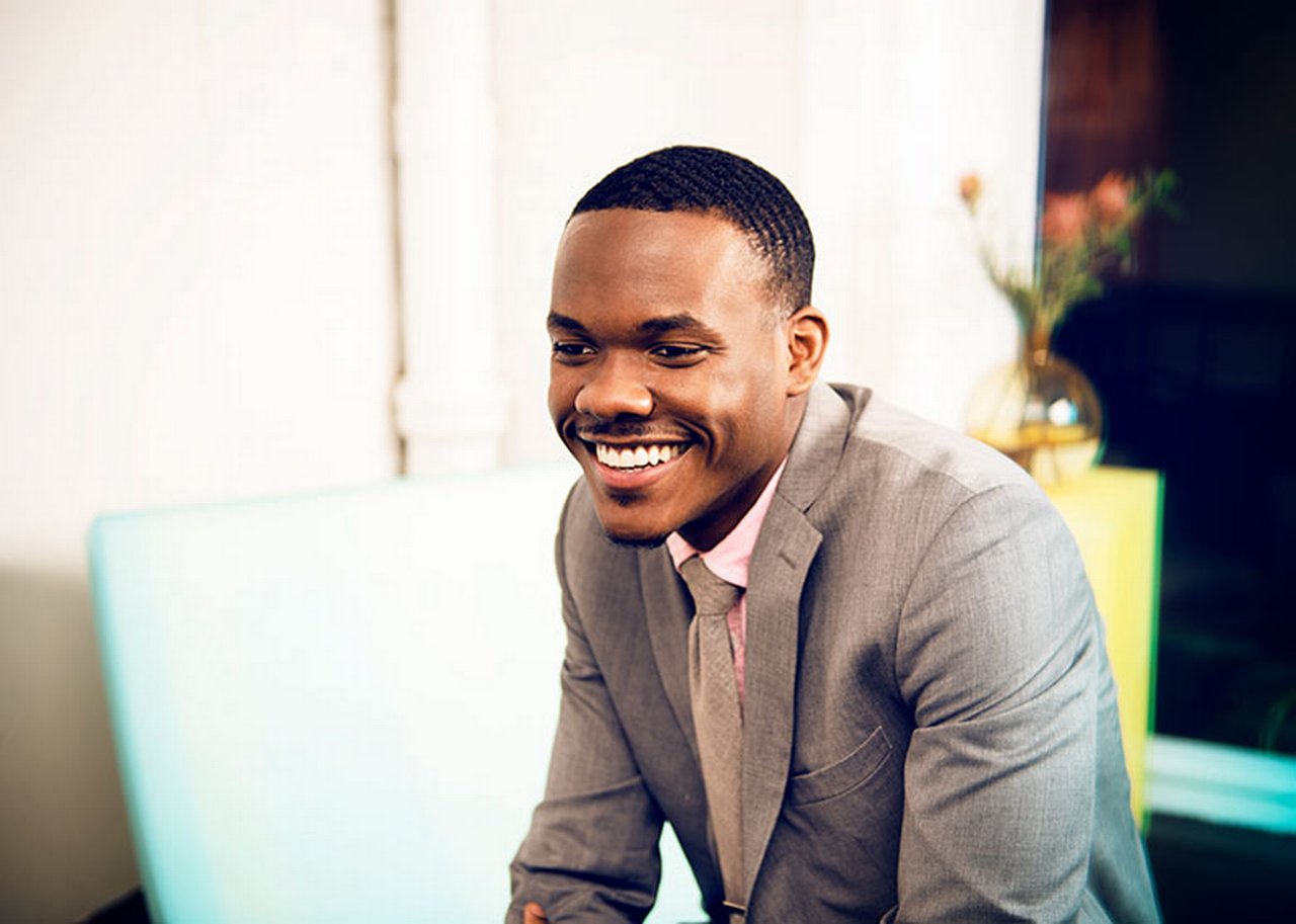 A man in a suit and tie. In the background a vase of flowers.