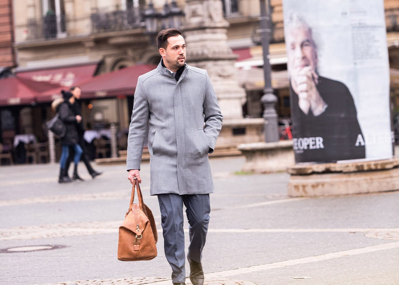 Semi is outside walking by a column with a bag in his hand