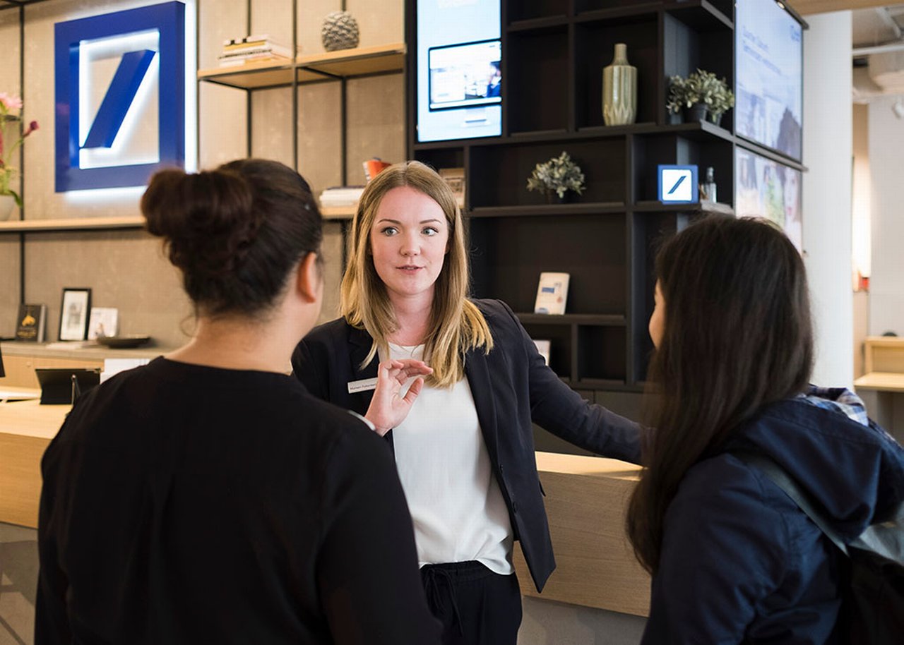 Marleen und zwei Kolleginnen unterhalten sich im Empfangsbereich. Im Hintergrund ist das Deutsche-Bank Logo zu sehen
