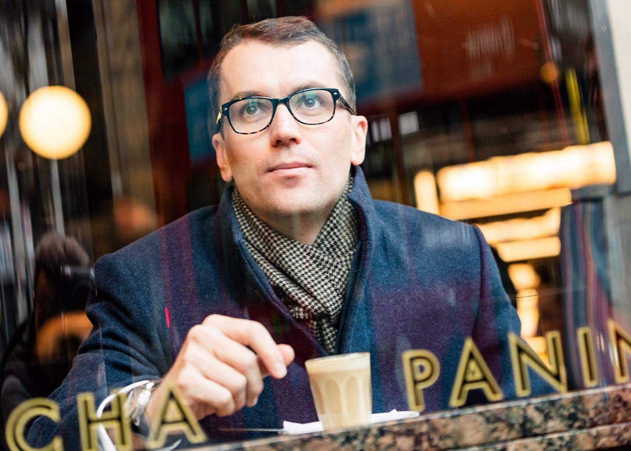 Mike is sitting in a cafe with a cup of coffee