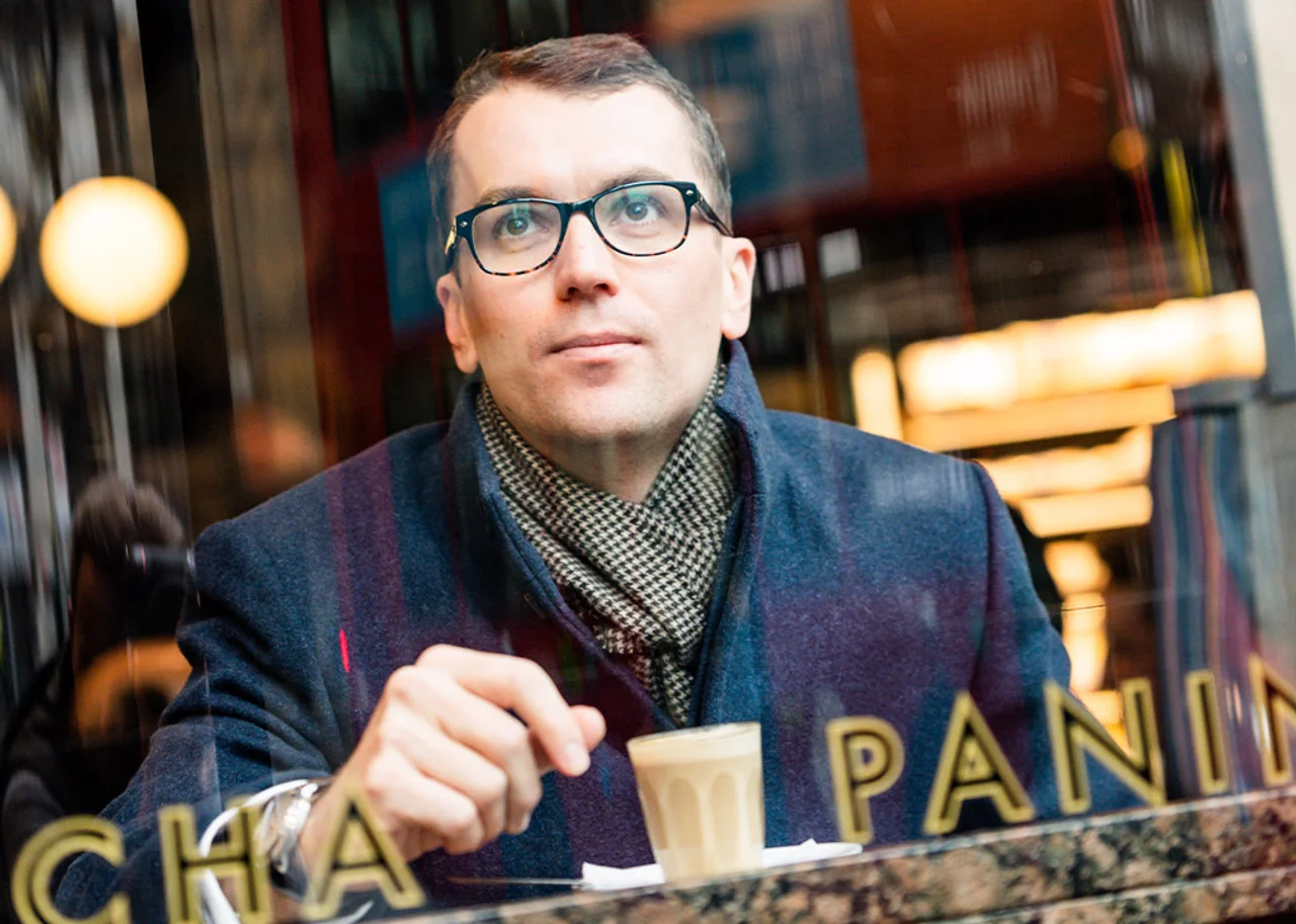 Mike is sitting in a cafe with a cup of coffee