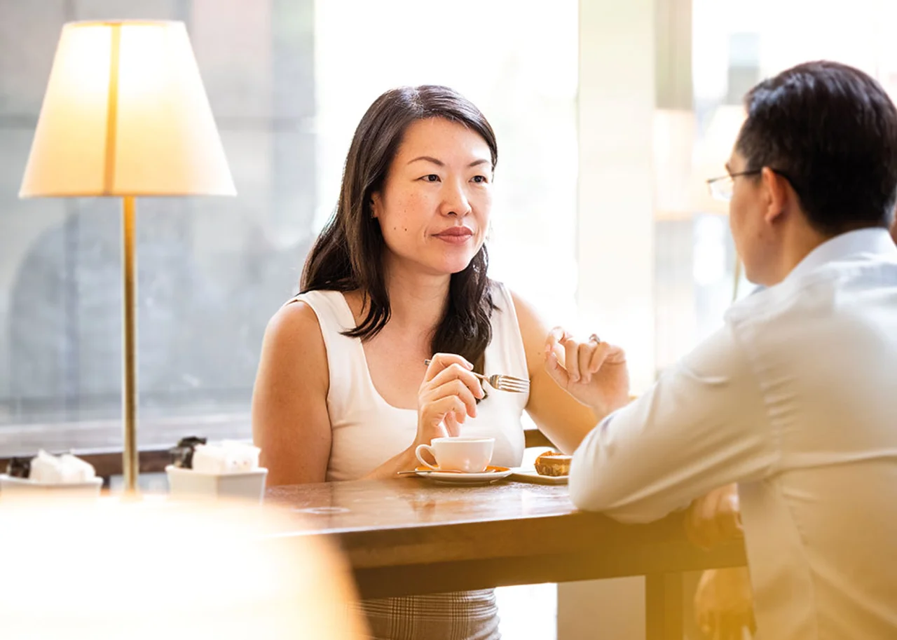 Wei Wei is sat at the table having a cup of Tea in conversation with a companion