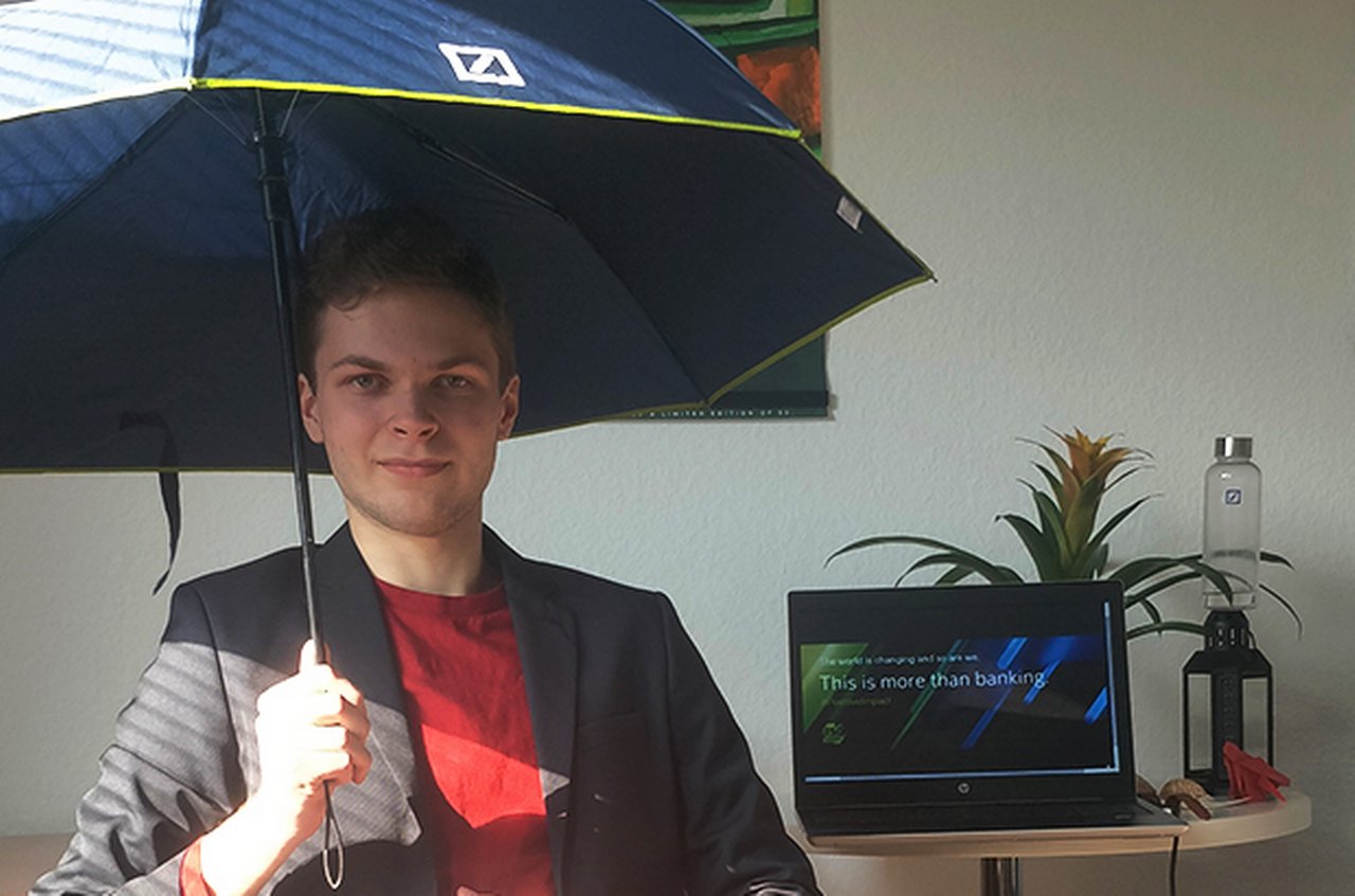 Luca sitzt im Büro und spannt einen Regenschirm mit Deutsche-Bank-Logo auf