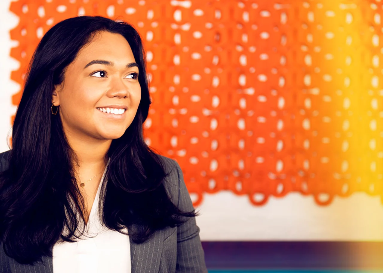 Camila lächelt vor einem orangenen Vorhang