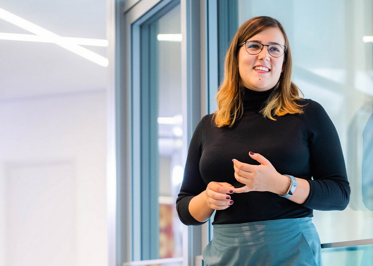 Iulia lächelt im Stehen und hält ihren kleinen Finger
